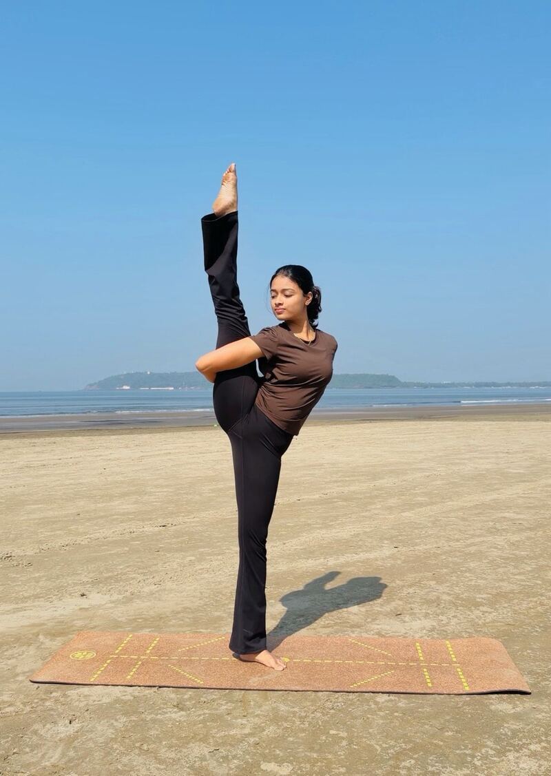 Akshata holding a standing split on the beach